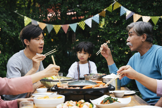 一个亚裔家庭在院子里一起吃泰国烤肉。