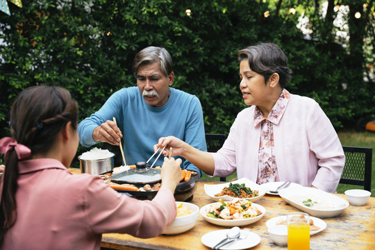 亚洲长辈夫妇和家人一起在院子里用筷子吃烧烤。