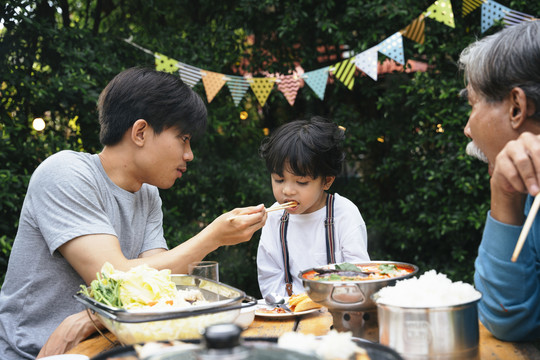亚裔父亲在户外聚餐会上给儿子喂食。