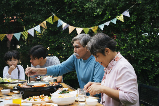 亚洲老年夫妇喜欢和家人一起在院子里吃泰国烧烤。
