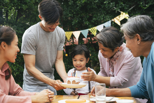 亚洲家庭在户外用蛋糕为孩子庆祝生日聚会。