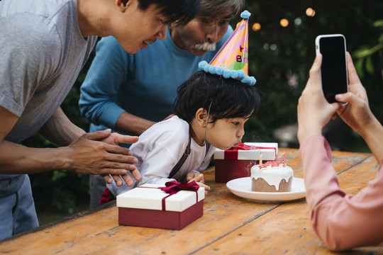 亚洲小孩吹蛋糕蜡烛与家人庆祝生日聚会。