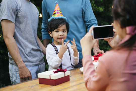 亚洲小孩在户外和家人一起庆祝生日聚会。妈妈用智能手机拍照。