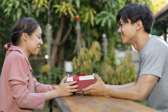 亚洲夫妇在户外互相赠送情人节礼盒的侧视图。