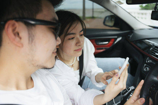 一对亚洲夫妇坐在车里，用智能手机上的地图应用程序。