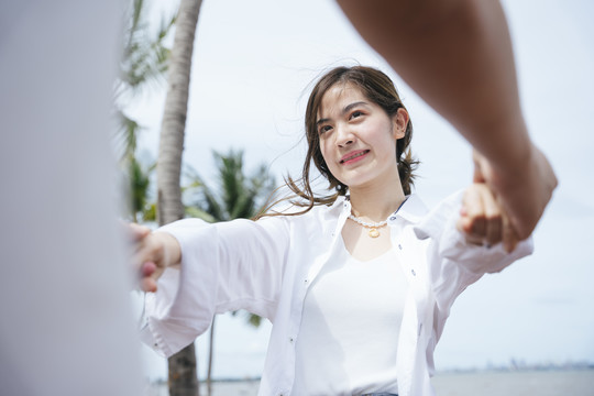 夏天，美丽的亚洲女人牵着男友的手在沙滩上跳舞。