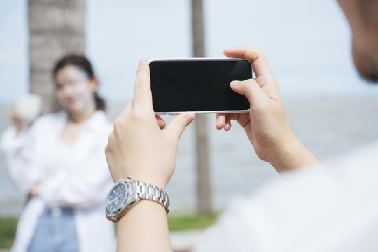 一名男子在沙滩上用智能手机给女友拍照。