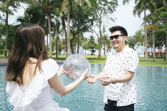 一对亚洲夫妇在游泳池玩塑料球。