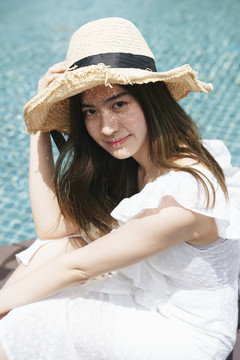 美丽的亚洲女子在游泳池戴着帽子，穿着白色连衣裙的肖像。