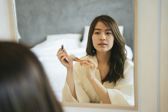 美丽的亚洲女人在卧室里用化妆粉擦脸颊。