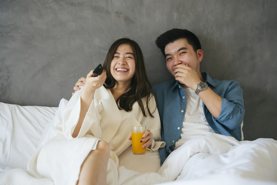 亚洲夫妇喜欢在酒店的卧室里一起看电视。