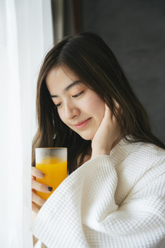 美丽的亚洲女人喝健康的新鲜橙汁。