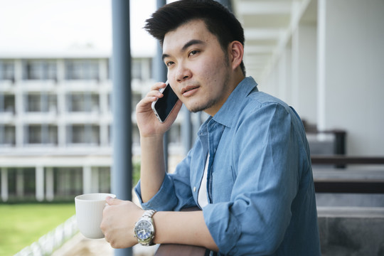 穿着蓝领衬衫的亚洲商人在酒店阳台上打电话。