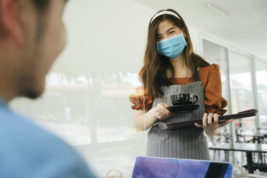 亚洲女服务员戴口罩给顾客端咖啡杯。