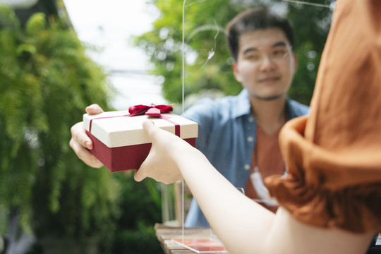 一个亚洲男人在户外院子里用礼盒给女友一个惊喜。他穿过障碍物送礼物。