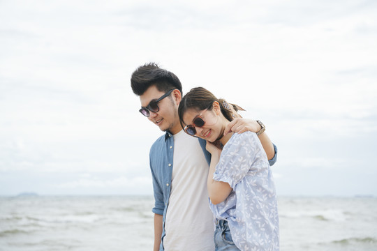 浪漫的亚洲情侣旅行者肩并肩走在沙滩上。