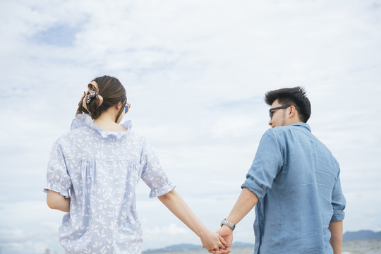 后视图-亚洲情侣旅行者手牵手在海滩上的夏天。