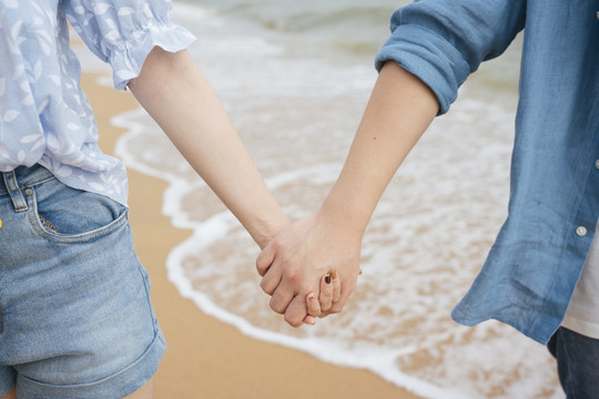 特写-亚洲情侣在沙滩上手牵手。