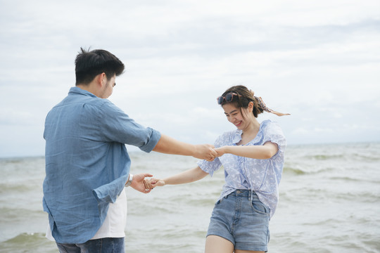 快乐浪漫的亚洲情侣旅行家牵手在沙滩上跳舞在夏天。