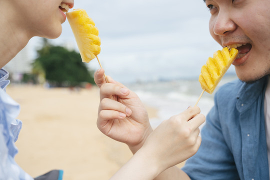 特写快乐的亚洲情侣旅行者在海滩上吃菠萝。
