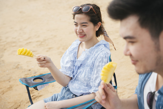 美丽的亚洲年轻旅女喜欢和男朋友在沙滩上吃菠萝。