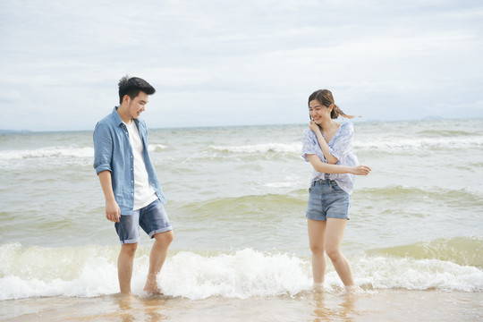 亚洲情侣旅行者在沙滩上玩泼水游戏。