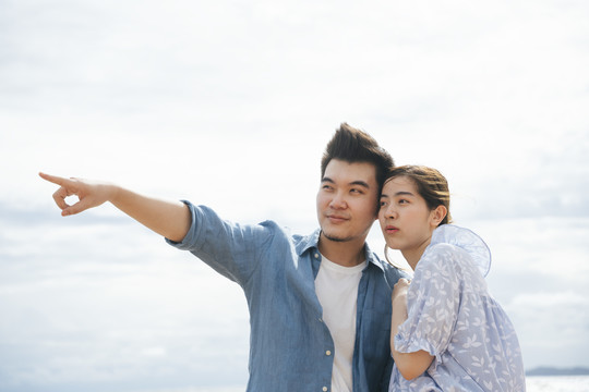 一对亚洲情侣在沙滩上用指点的姿势旅行。