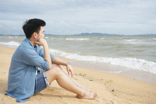 孤独的亚洲人在夏天独自坐在沙滩上看海。