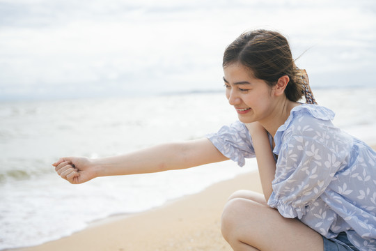 美丽的亚洲女人在沙滩上抓一堆沙子。