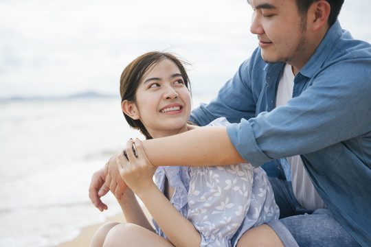 美丽的亚洲女人回头看着她的男朋友在沙滩上拥抱她。