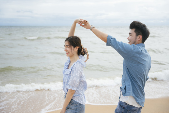 快乐的亚洲情侣在沙滩上跳舞。