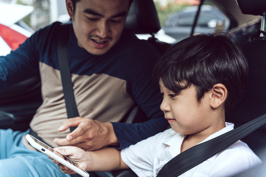 亚裔父亲教儿子如何在车上使用安全带。