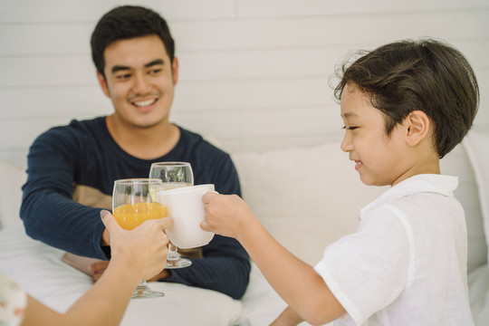快乐的亚泰家庭一起用橙汁杯和牛奶杯欢呼。父母和儿子用健康饮料敬酒。