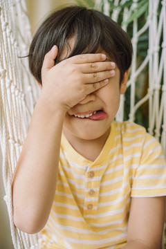 特写肖像-快乐的亚泰男孩遮住眼睛，伸出舌头。
