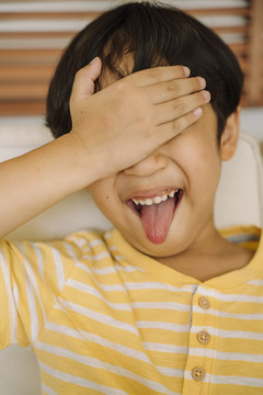 特写肖像-快乐的亚泰男孩遮住眼睛，伸出舌头。