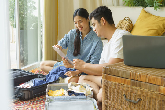 亚泰家庭预订酒店和航班，使用数字笔记本电脑。行李箱里有几件行李。