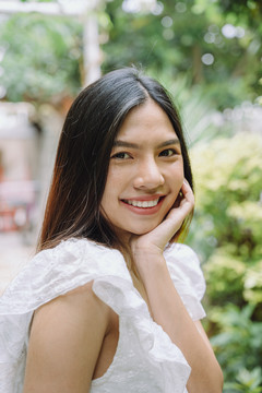 在公园里，一位身着白色连衣裙的快乐的亚洲黑发泰国妇女的肖像。