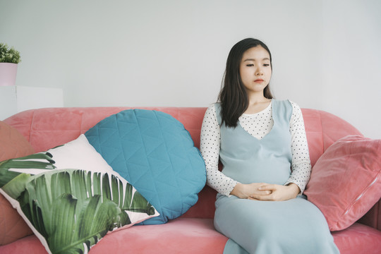 年轻漂亮的亚洲孕妇在客厅的粉色沙发上休息。