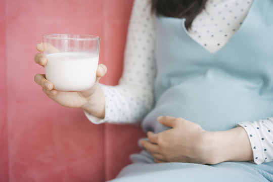 亚洲年轻漂亮孕妇手捧肚子和一杯牛奶。复制空间。