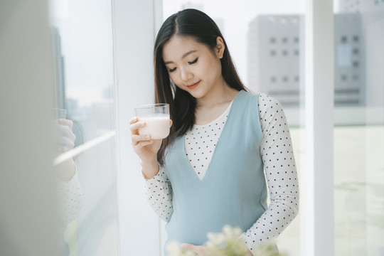 年轻漂亮的亚洲孕妇端着一杯牛奶。妈妈的健康饮料。