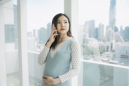 年轻漂亮的泰国亚裔孕妇在家使用智能手机。