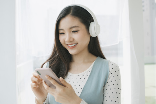 特写肖像-年轻美丽的亚洲孕妇用智能手机耳机听音乐。