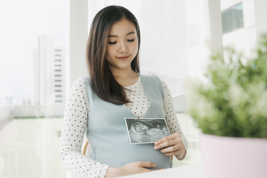年轻漂亮的亚洲孕妇在家里抱着宝宝做x光超声扫描。
