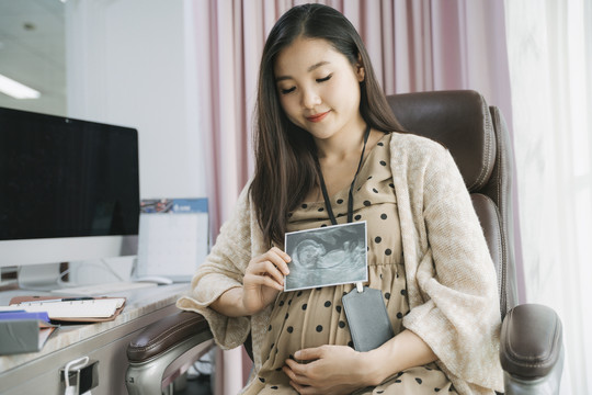 美丽怀孕的亚洲女商人在办公室工作时看超声波x光扫描。