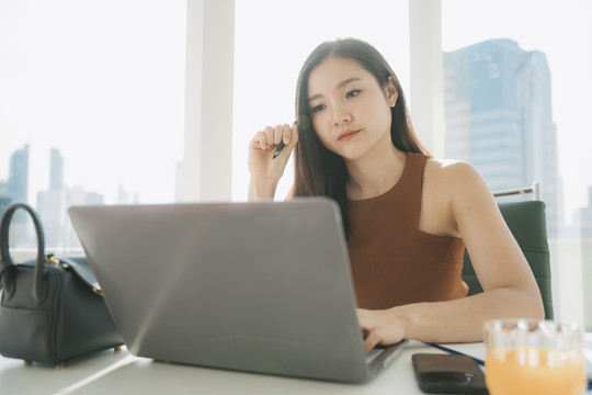 体贴美丽的亚泰女商人在办公室工作的地方用笔记本电脑工作。