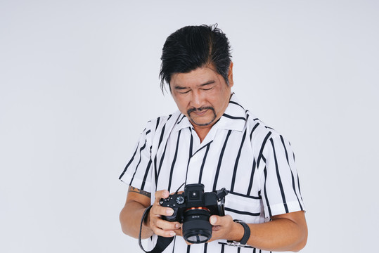 穿着白衬衫的亚洲成年男子，在白色背景上用相机拍摄。
