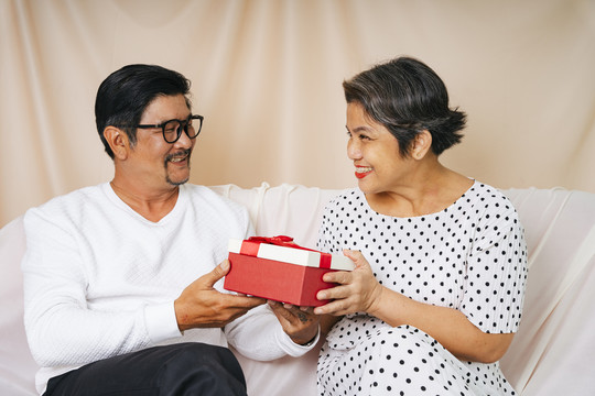 浪漫的老年夫妇在沙发上送生日快乐礼盒。