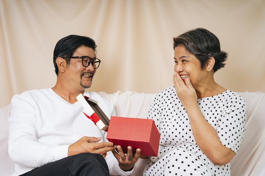 浪漫的老年夫妇在沙发上送生日快乐礼盒。