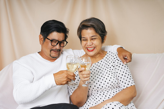 一对亚洲老夫妇坐在沙发上用酒杯庆祝。