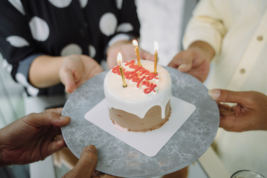 生日快乐蛋糕与蜡烛与人们的手包围。